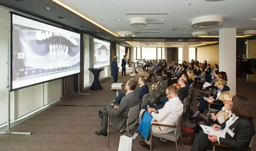 Una sala de conferencias llena durante una ponencia, con una radiografía proyectada en la pantalla